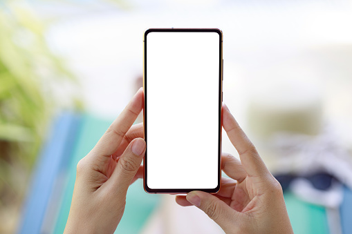 A mockup smartphone held by a woman against the backdrop of a tropical resort. This image represents travel and outdoor recreation. It shows how smartphones seamlessly integrate into our adventures, enhancing our travel experiences.