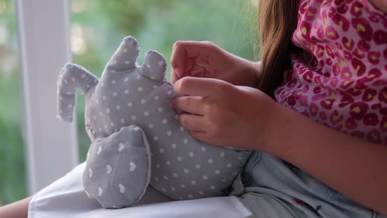 Close-up of a child's hands sewing a soft toy. The girl sews up a soft toy of an elephant. Handmade, hobby.