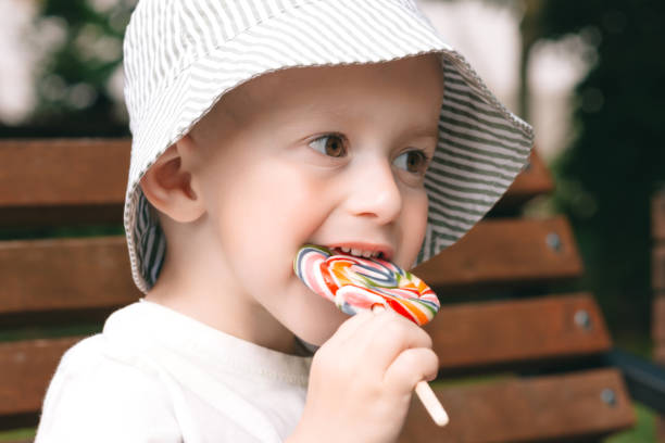 istock A boy in panama gnaws a multi-colored lollipop on a bench. Sweets are bad for teeth. 1698774994