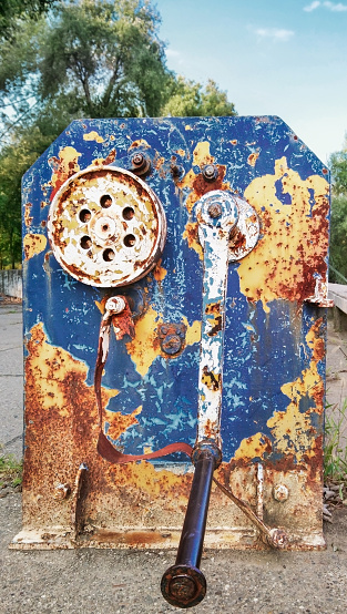 High resolution Image of an grunge old decommissioned, badly corroded, rusty, heavy duty manual marine winch, with its yellow blue paint cracked, exfoliated and partially peeled off.
