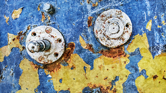 High resolution Image of an grunge old decommissioned, badly corroded, rusty, heavy duty manual marine winch detail, with its yellow and blue paint cracked, exfoliated and partially peeled off.