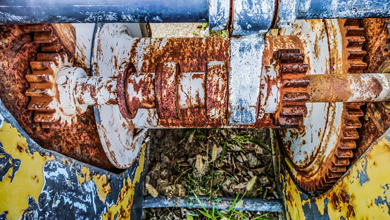 High resolution Image of an grunge old decommissioned, badly corroded, rusty, heavy duty manual marine winch detail, with its yellow and blue paint cracked, exfoliated and partially peeled off.