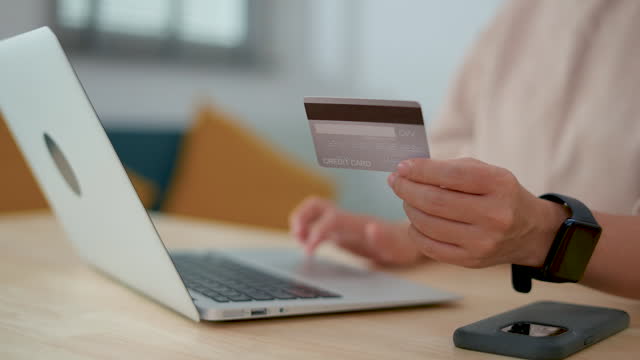 Close up shot of female hand holding credit card using laptop for shopping online at home office.