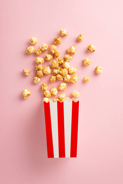 istock Film Fanatic's Dream: A vertical top view of popcorn spilling from a striped box on a soft pink surface, perfect for text or advertising 1698846246
