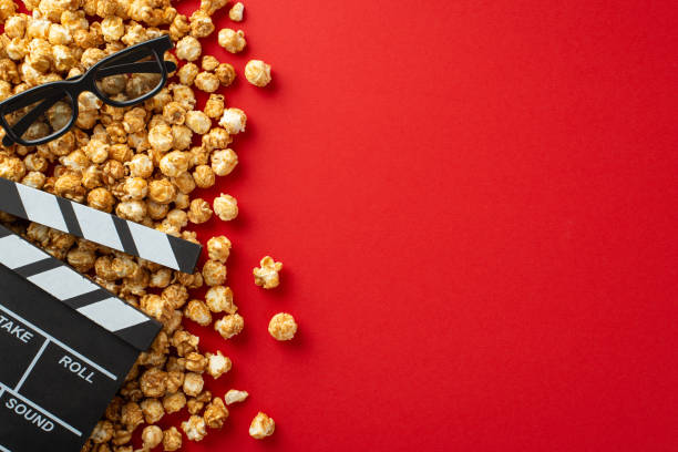 istock Top view image of numerous popcorn kernels, 3D glasses, and a clapperboard on red surface, ideal for text or advertising 1698846248