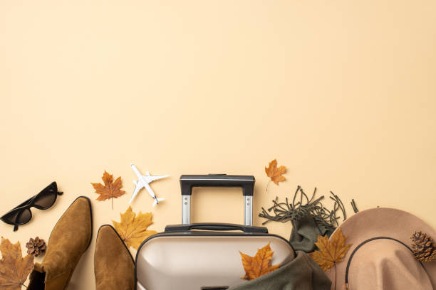 istock Fall vacation mood. Top view with elegant gray suitcase, maple leaves, felt fedora hat, boots, sunglasses and warm scarf on a beige isolated background, perfect for your travel message or ad 1698846339