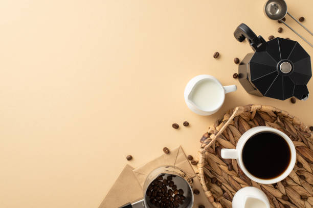 istock Commemorate Coffee Day with striking setup. Top view of scattered coffee beans, espresso cup within elegant wicker tray, milk, cream jars, etc on pastel beige surface, offering space for your message 1698846372