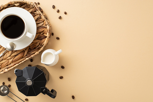 Savor the moment on Coffee Day: top view of roasted beans, espresso mug in wicker tray, milk jar, spoon, and kettle on pastel beige background â add your text or logo