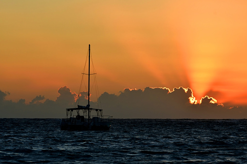 Anchored Boat with Sun Peeking Over the Clouds at Sunrise on a Ocean