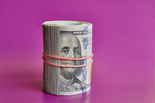 istock Many hundred dollar bills rolled up with a red rubber band on a colored background. 1698882008