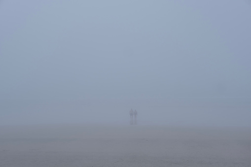Two wild swimmers exit the sea in fog, Devon UK