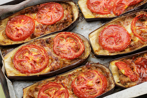 Meat stuffed eggplant boats with melted cheese and slices of tomato
