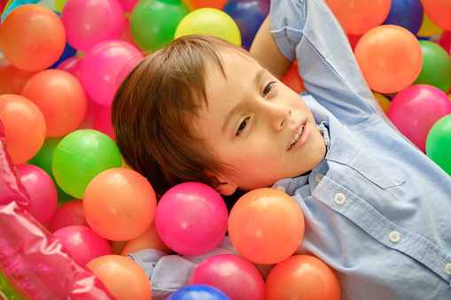 Little smiling boy playing in a pool of colored balls of many colors.