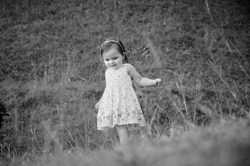 Black and white photograph of a three year old girl walking through a meadow in the countryside.