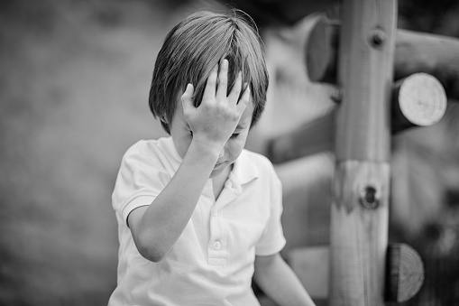 Photograph in black and white of a child holding his head in his hand as a sign of concern.