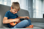 Cute little boy tuning little guitar on a sofa