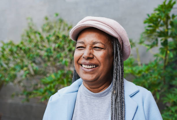 portrait of happy senior african woman wearing trendy hat and smiling in front of camera during winter time - life events laughing women latin american and hispanic ethnicity imagens e fotografias de stock