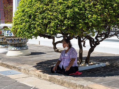The hot and humid weather in Bangkok, Thailand, can be difficult even for the locals. A Thai woman is resting in the shade under a tree at the Wat Arun Temple.