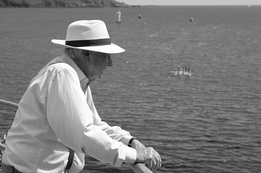 Plymouth, Devon, England: July 07 2022: Black and white photography. An elderly, well dressed man standing on the promenade looking out to sea