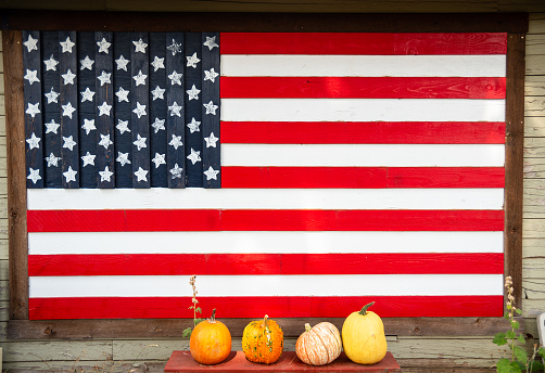 Autumn background for the holiday Halloween. Pumpkins lined up on a bench under an USA flag painted on a wooden wall. Pumpkin decoration concept for Halloween
