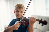 Happy little boy practicing violin at home