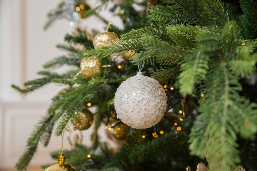 Christmas tree with vintage acorn and baubles with golden lights close up. Modern decorated christmas tree branches with stylish ornaments in festive room. Winter holidays, atmospheric time