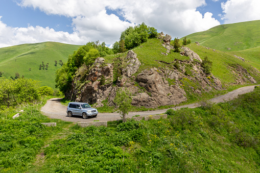 4x4 car driving on M-20 winding gravel road towards Tskhratskaro Pass, Georgia with Trialeti (Caucasus) mountains and green grasslands around.