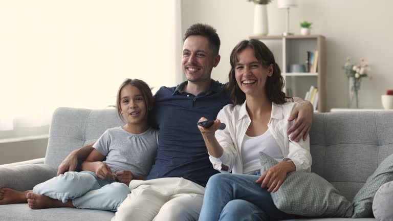 Happy young parents and preschool daughter kid watching TV