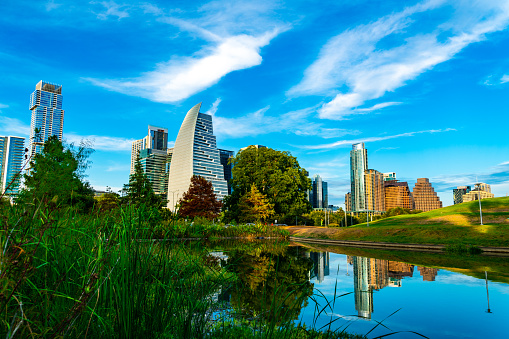 Mirrored Lake Reflections of Austin Texas Cityscape and modern skyscrapers with green nature pond views of Downtown Skyline and blue sky and a few wispy clouds