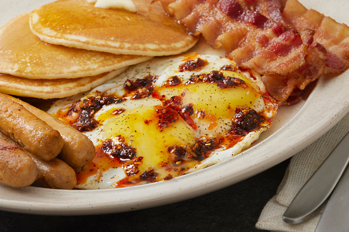 Spicy Chili Crisp Breakfast with Sunny side up eggs, Pancakes, Bacon, Sausages, Toast, Orange Juice and Coffee