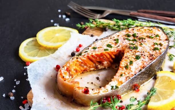 istock Fried salmon steak with thyme and lemon served on wooden plate on black table. 1699045964
