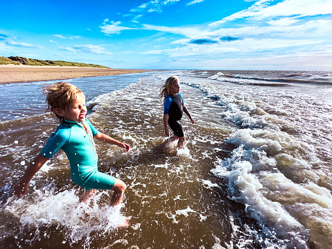 Happy children playing in the sea. Happy kids running in the waters. Children embracing waves on the beach. Summer vacation and healthy Lifestyle concept. Children having fun on the beach. Healthy lifestyle concept. Spring break