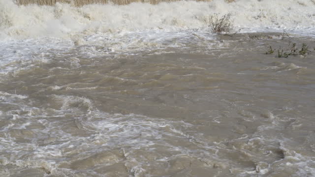 The river swollen after heavy rainfall and flood water crashing through valley. The water flows fast from the high valley to the plain. General contest of a river in flood