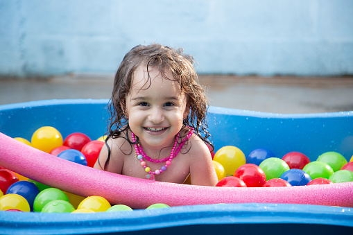Goiânia, Goias, Brazil – July 17, 2023:  A happy child in a plastic pool with water and colorful balls.
