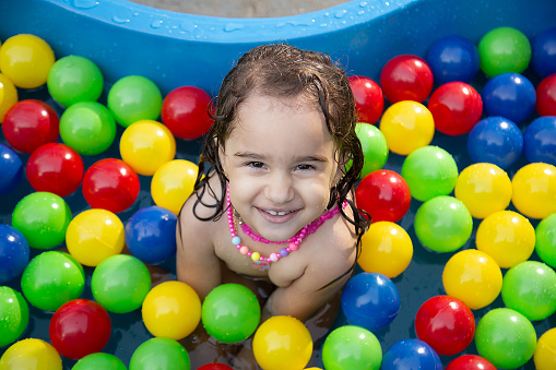 Goiânia, Goias, Brazil – July 17, 2023:  A happy child in a plastic pool with water and colorful balls.