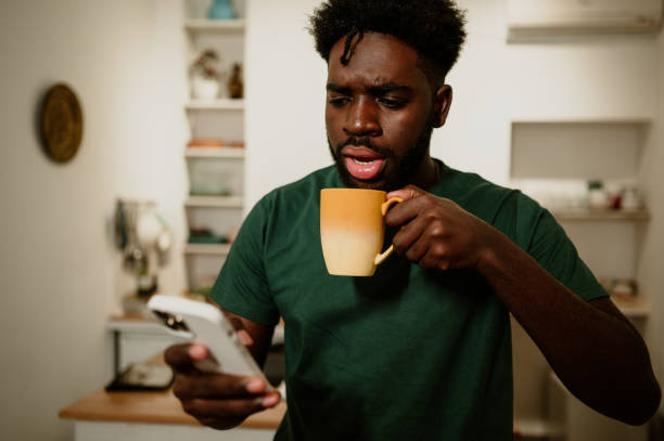 istock An african american serious man is reading a phone message while drinking coffee at home. 1699088465