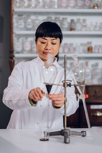 A professional Japanese chemist in a lab coat is making a liquid drug while standing in a pharmacy. A pharmacist is making a liquid traditional alternative drug in the apothecary.