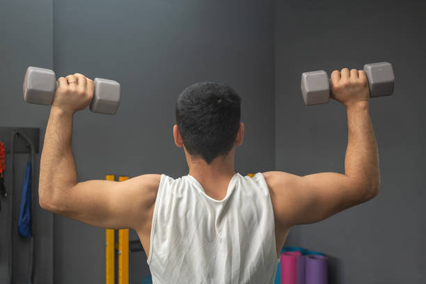young athlete doing shoulder press overhead in front of the mirror. - body building determination deltoid wellbeing imagens e fotografias de stock