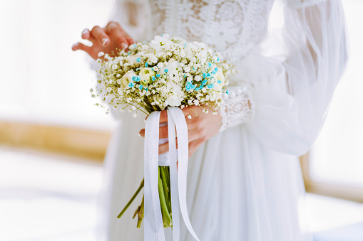Unrecignizable bride in white dress holding bouquet close up