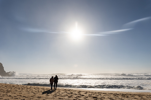 28 February 2023 Nazare, Portugal: A couple standing on the beach and looking at the ocean in cold weather. Mid shot