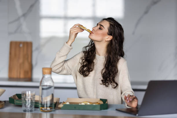 istock Young woman taking a break and eating pizza, working from home on laptop 1699103737
