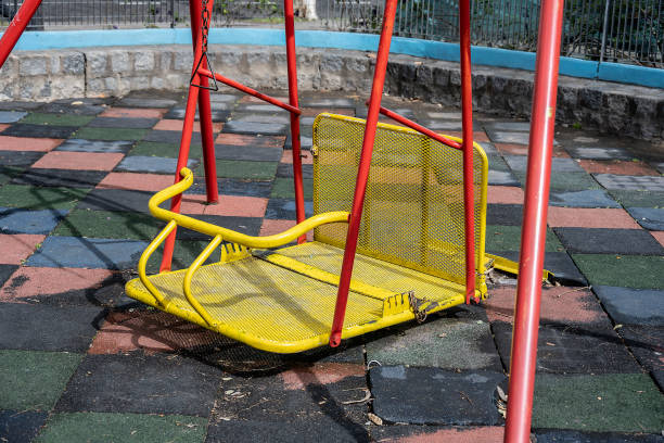 The covering is damaged on the old playground under the swings on a chain. Hole in pressed rubber crumb tiles