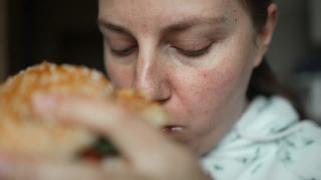 Caucasian woman eating burger. Female biting yummy cheeseburger, close up. Slow motion.