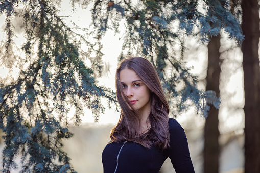 A girl stands near a blue spruce in an autumn park