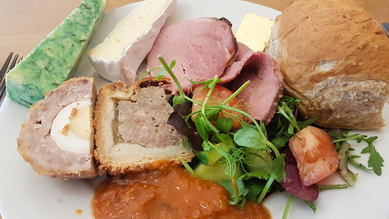 Ploughman's Lunch, ham, scotch egg and pork pie and all the trimmings a tasty healthy lunch set out ready to eat in café