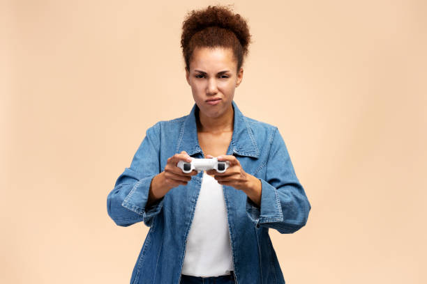 excited ethnic woman in casual denim, plays computer games with joystick, isolated beige background - racing game imagens e fotografias de stock