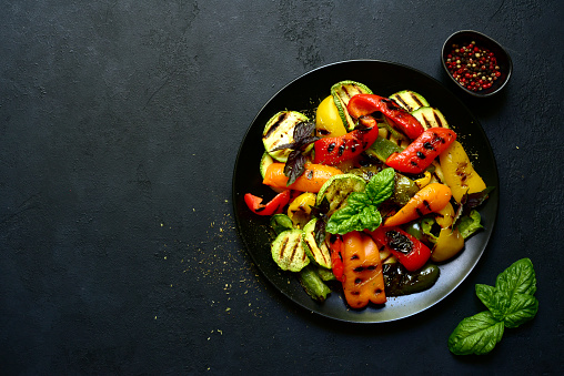 Grilled colorful vegetable : bell pepper, zucchini, eggplant on a  black plate over dark  slate, stone or concrete background. Top view with copy space.