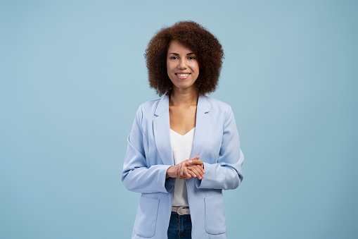 Successful african american female entrepreneur standing and looking at the camera isolated on blue background. Happy smiling businesswoman in suit posing
