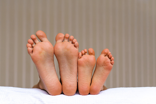 Small and large bare feet, two pairs of barefoot close-up, children lying on the bed. Foot Relaxing. Togetherness and Growing up concept. Childhood moments.