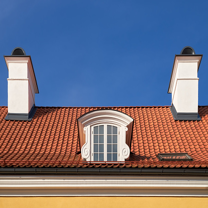 Old vintage garret roof with window and chimneys. Retro attic window and fireplace chimneys, Riga, Latvia.